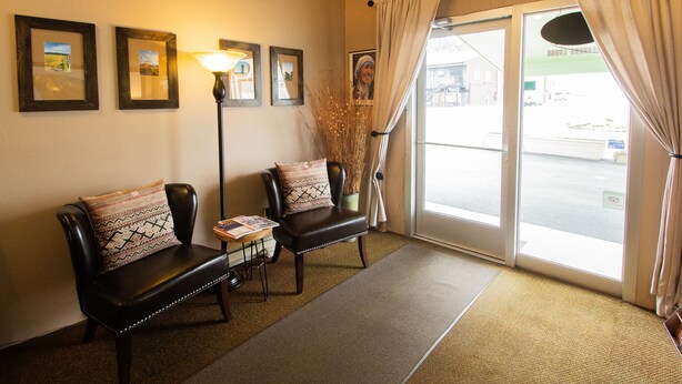A reception area with two leather chairs, a lamp, framed pictures on the wall, and a view through the door. - Dreamers Lodge (John Day)