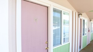 A row of pastel-colored doors with numbers indicating room assignments, leading to a corridor with windows and doors. - Dreamers Lodge (John Day)