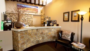 A reception area with a stone counter, a black leather chair, a lamp, framed pictures, and a large vase with branches. - Dreamers Lodge (John Day)