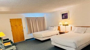 A hotel room with two beds, a desk with a chair, a door, and a window with curtains. - Dreamers Lodge (John Day)