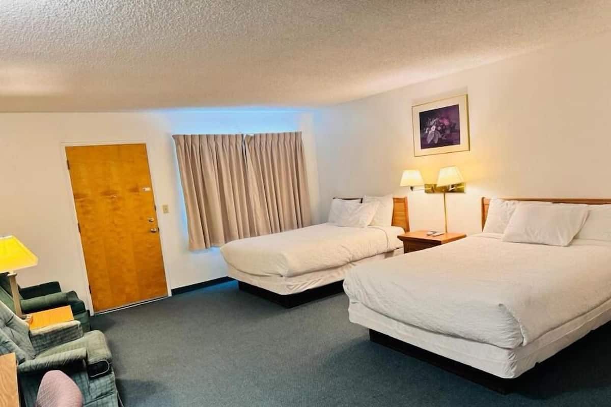 Een hotelkamer met twee bedden, een bureau met stoel, een deur en een raam met gordijnen.