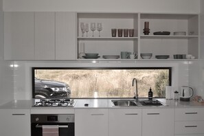 A modern kitchen with a large window, stainless steel appliances, and neatly organized shelves with glassware and dishes.