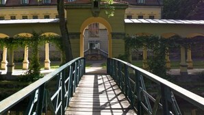 Un pont de fusta que condueix a un edifici amb façana groga i teulada de teules vermelles.