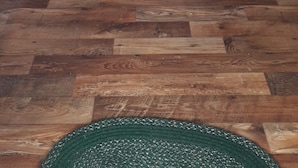 Una habitación con piso de madera, un televisor sobre un mueble de madera, una silla de mimbre y una puerta que da a otra habitación.