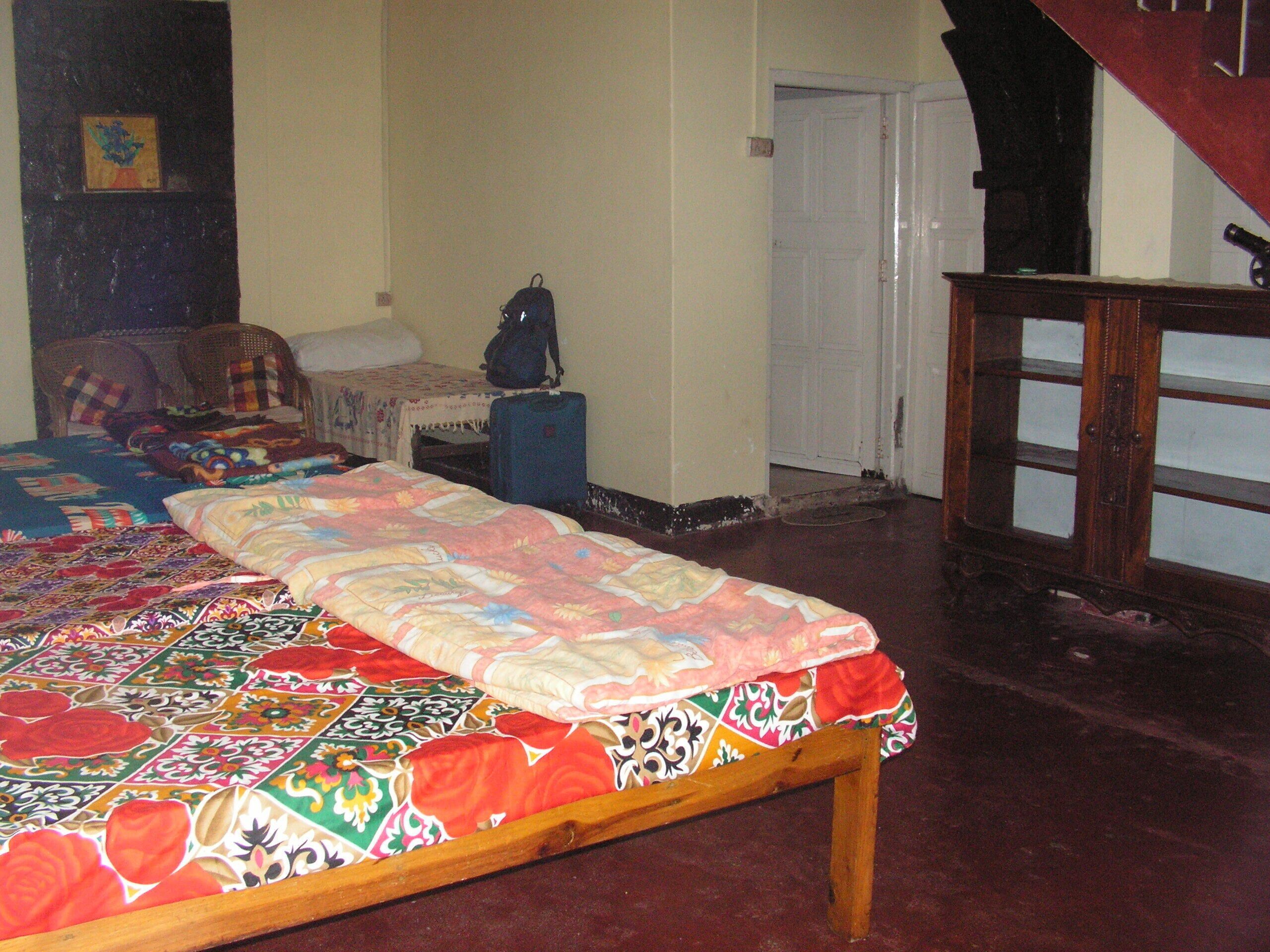 A bedroom with a bed, a suitcase, a chair, and a door.