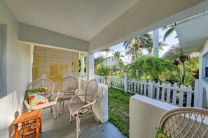 A covered outdoor seating area with wicker chairs and a small table, a white picket fence, and lush greenery in the background. - BeachTrail Lodging (Indian Rocks Beach)