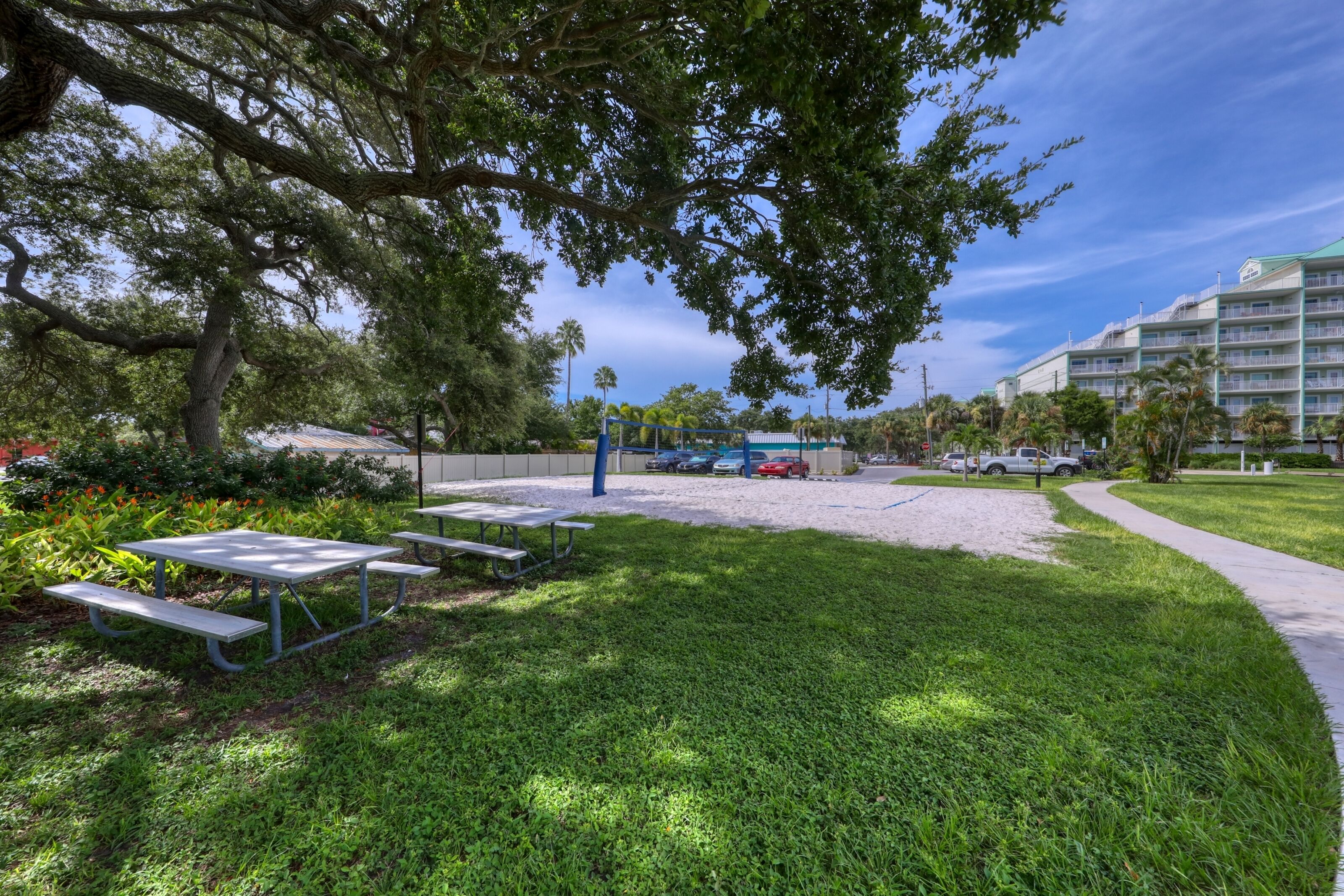 A grassy area with picnic tables and a parking lot with cars.