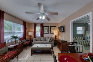 Un salon avec un ventilateur de plafond, un canapé, une table basse, un téléviseur et un lit avec une literie à rayures.