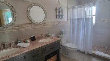 A bathroom with a double sink vanity, a toilet, a shower with a curtain, and a mirror with decorative frames.