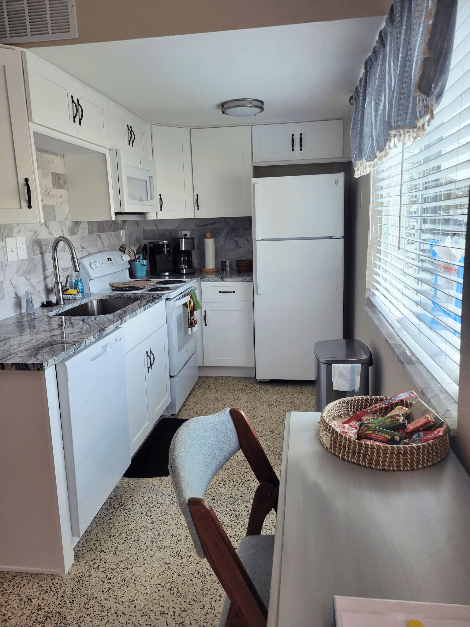 A compact kitchen with white cabinets, a built-in microwave, a refrigerator, and a sink.
