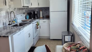 A compact kitchen with white cabinets, a built-in microwave, a refrigerator, and a sink.