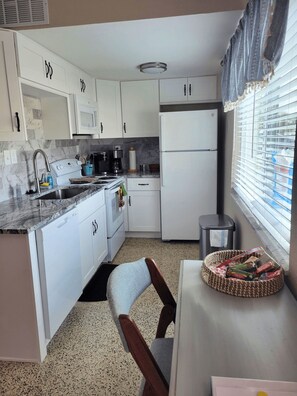 Una cocina compacta con armarios blancos, microondas integrado, refrigerador y pileta.