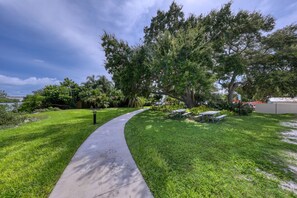 A curved concrete pathway leading to a picnic area with benches, surrounded by lush green grass and trees. - BeachTrail Lodging (Indian Rocks Beach)