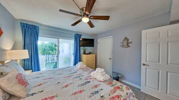 A bedroom with a bed, a ceiling fan, a TV, a dresser, and a door.