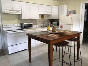 A kitchen with white cabinets, a stove, a microwave, and a refrigerator. There is a wooden table with two chairs and decorative items on it. - BeachTrail Lodging (Indian Rocks Beach)