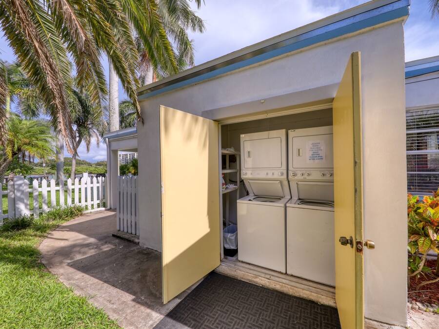 A laundry room with a door open, revealing washing machines and a small storage area.