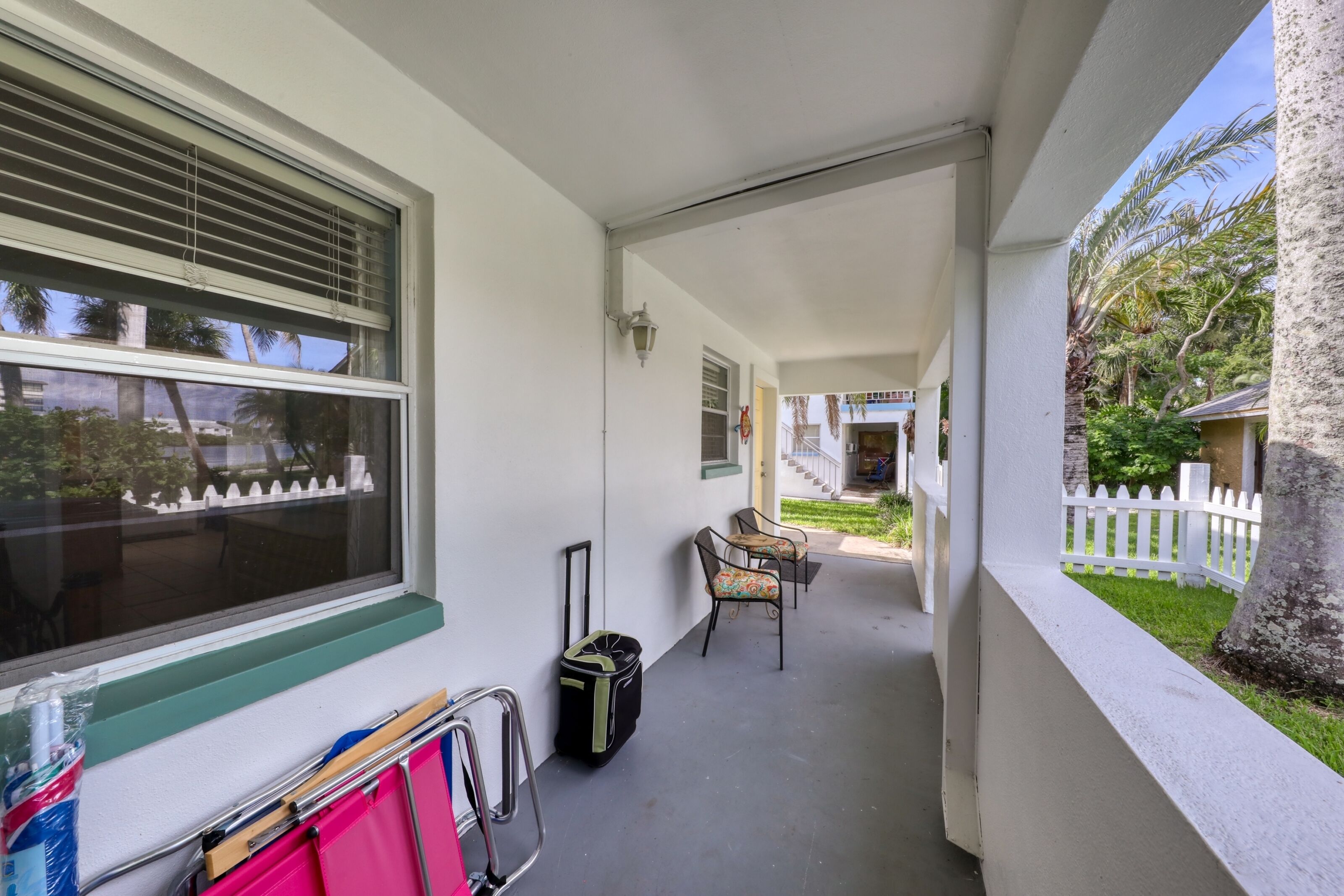 A covered porch with a window, a chair, a suitcase, and a small table.