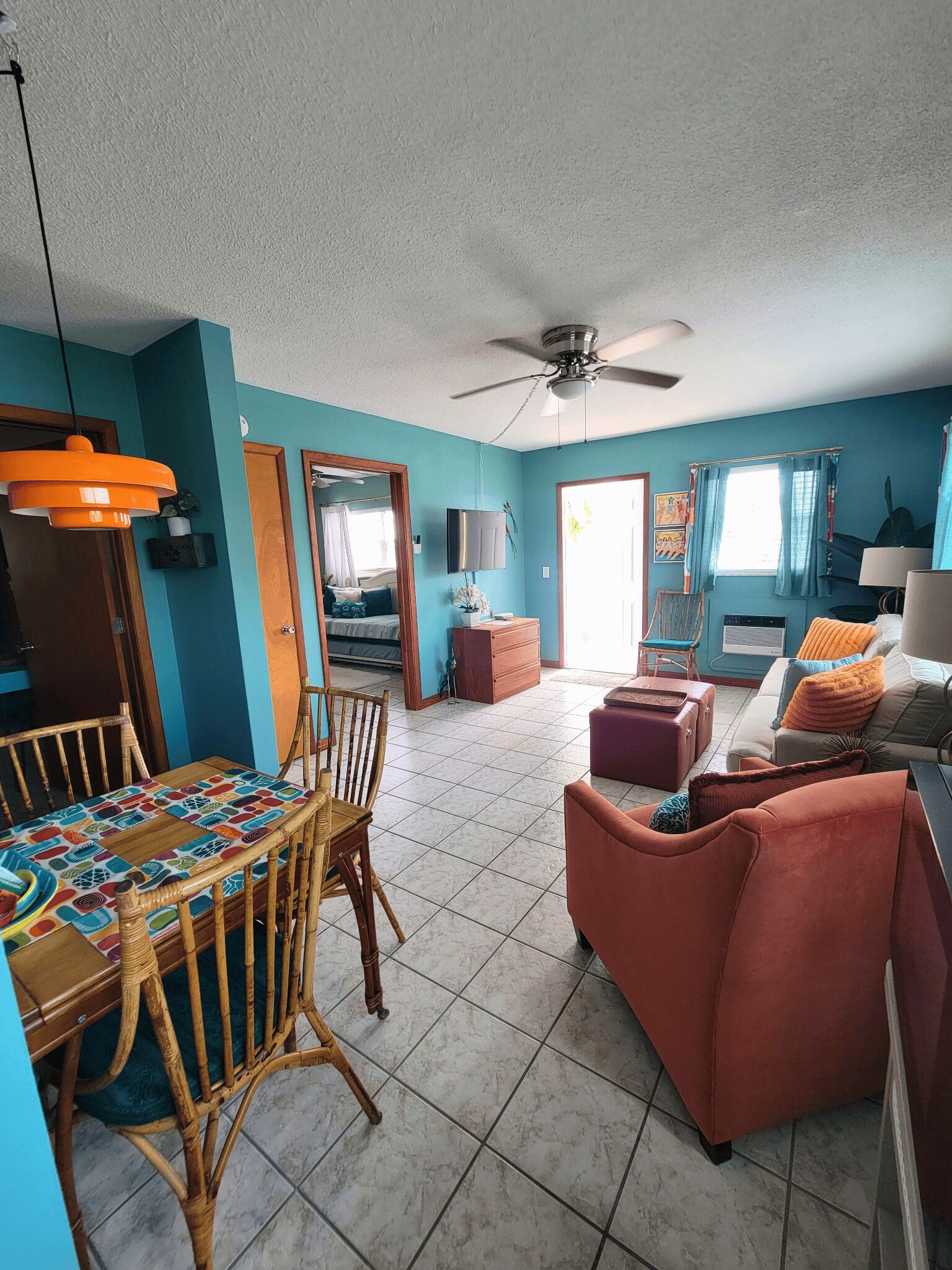 A spacious living room with a dining area, a ceiling fan, and a large window with curtains.