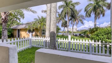 A white picket fence, palm trees, and a building with a yellow facade.