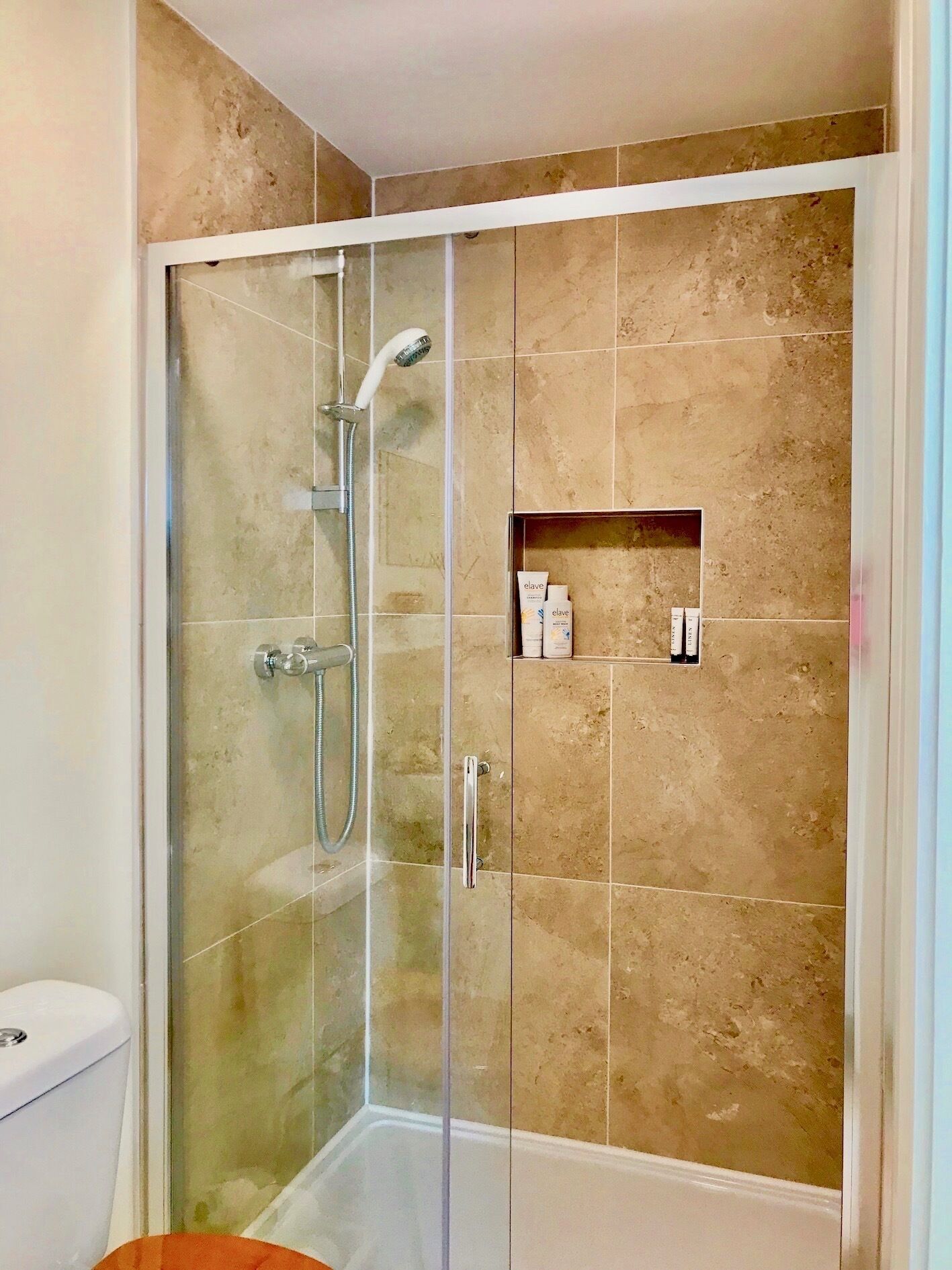 A glass-enclosed shower stall with beige tiles, a handheld showerhead, and a glass door.