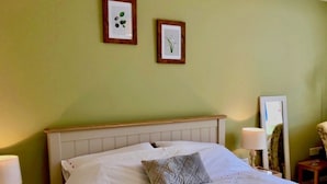Uma cama bem arrumada com lençóis brancos e um travesseiro cinza, uma cabeceira de madeira e duas gravuras botânicas emolduradas na parede.