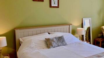 A neatly made bed with white linens and a gray pillow, a wooden headboard, and two framed botanical prints on the wall.