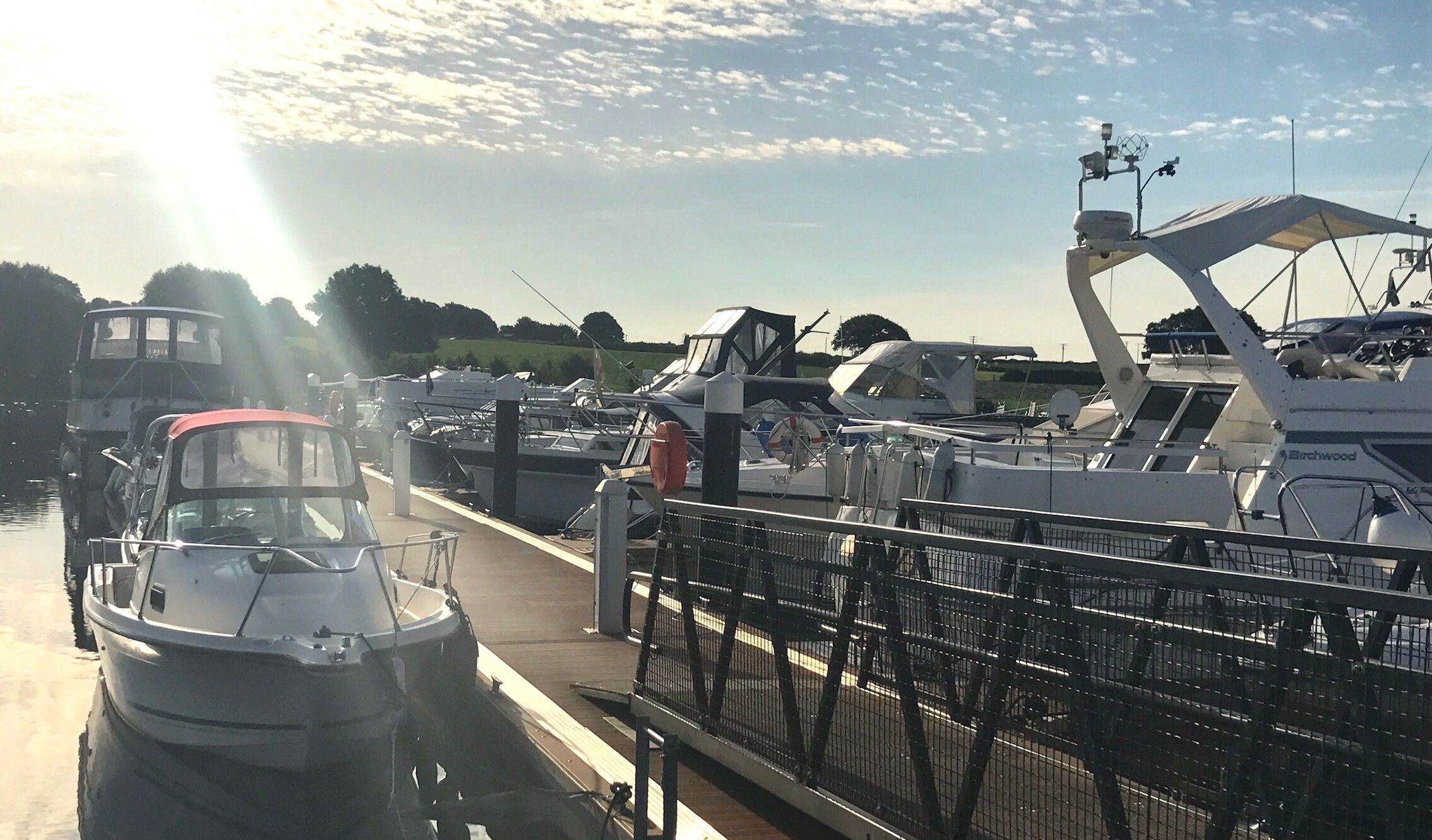 A marina with boats docked, a pedestrian walkway, and a clear sky.