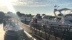 Uma marina com barcos atracados, um calçadão e céu claro.