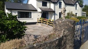 A two-story house with a stone pathway leading to the entrance, surrounded by greenery and a stone wall. - Ashside Cottage,  Royal Hillsborough, Belfast (Lisburn)