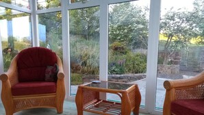 A room with wicker furniture, a glass table, and large windows offering a view of a garden. - Ashside Cottage,  Royal Hillsborough, Belfast (Lisburn)