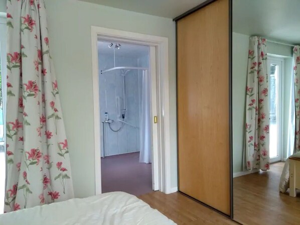 A bedroom with a bed, a wooden wardrobe, and a bathroom with a shower.