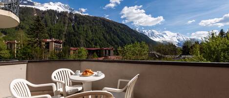 Una terrazza con tavolo e sedie, vista su un paesaggio montuoso con cime innevate.