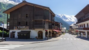 Un edificio de madera con un letrero de cafetería, una calle con pasos de cebra y montañas nevadas al fondo.