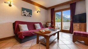 Una habitación acogedora con un sofá rojo, una mesa de madera con una bandeja, una televisión y vistas a las montañas a través de una puerta de cristal.