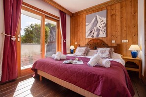Une chambre d’hôtel avec un grand lit, des murs lambrissés, un tableau et un balcon avec des rideaux rouges.