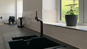 A modern kitchen with a black sink, a coffee machine, and a potted plant by the window. - Luxurious home in secluded location with rural views just 5 mins drive to beach  (Torpoint)