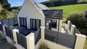 A modern house with a sloped roof, large windows, and a fenced patio area. - Luxurious home in secluded location with rural views just 5 mins drive to beach  (Torpoint)