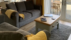 A modern living room with a grey sofa, a wooden coffee table, and a yellow throw blanket. - Luxurious home in secluded location with rural views just 5 mins drive to beach  (Torpoint)