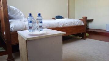 Quarto com duas camas de madeira, uma mesa de cabeceira branca com um copo e duas garrafas de água.