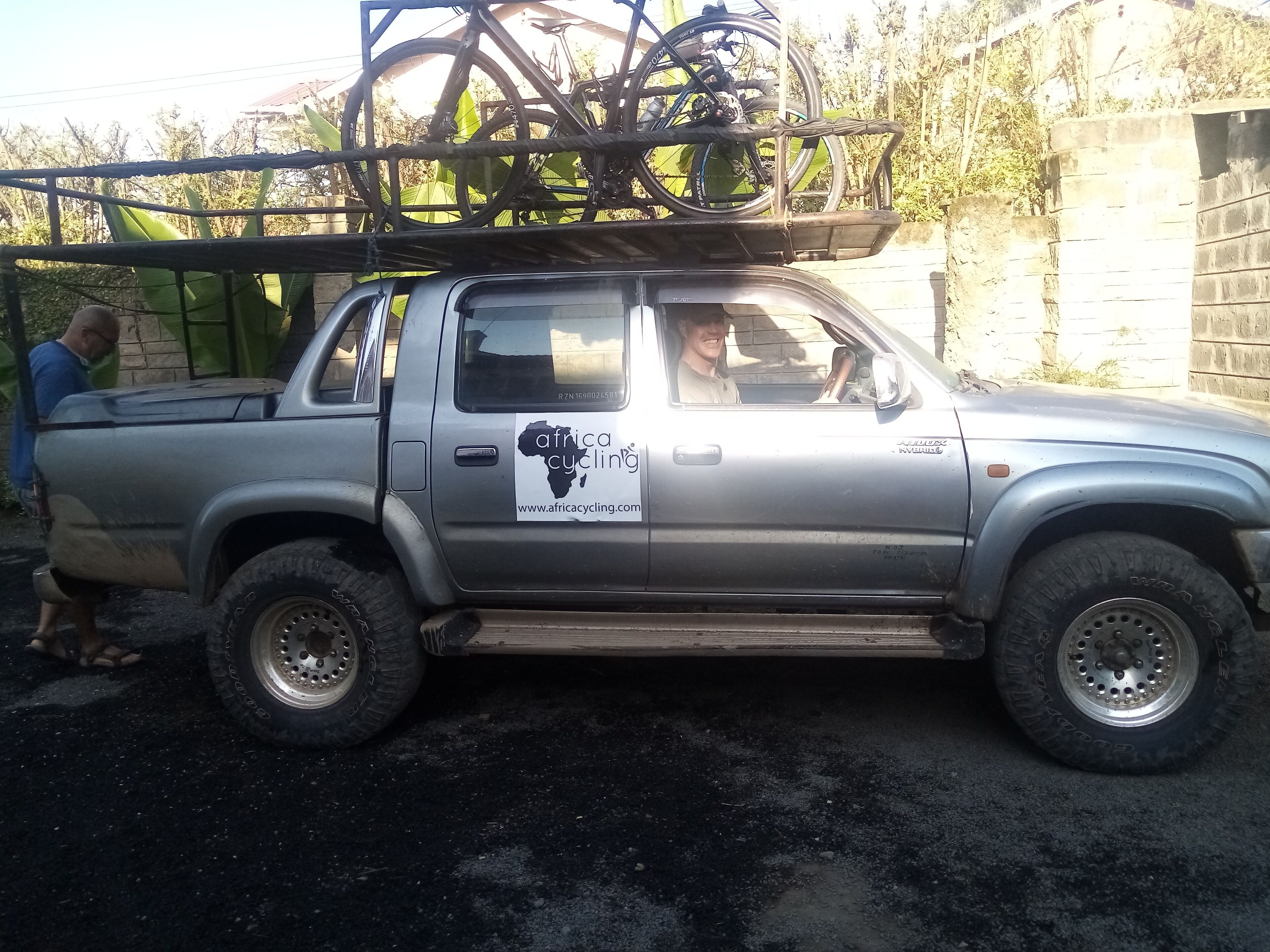 Un camionnette argentée, équipée d’un porte-vélos sur lequel sont fixés deux vélos, est garée devant un immeuble.