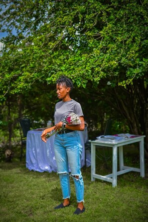 A person holding a bouquet of flowers in an outdoor setting with a table and a covered area in the background. - HomeBase Gardens (Nakuru)