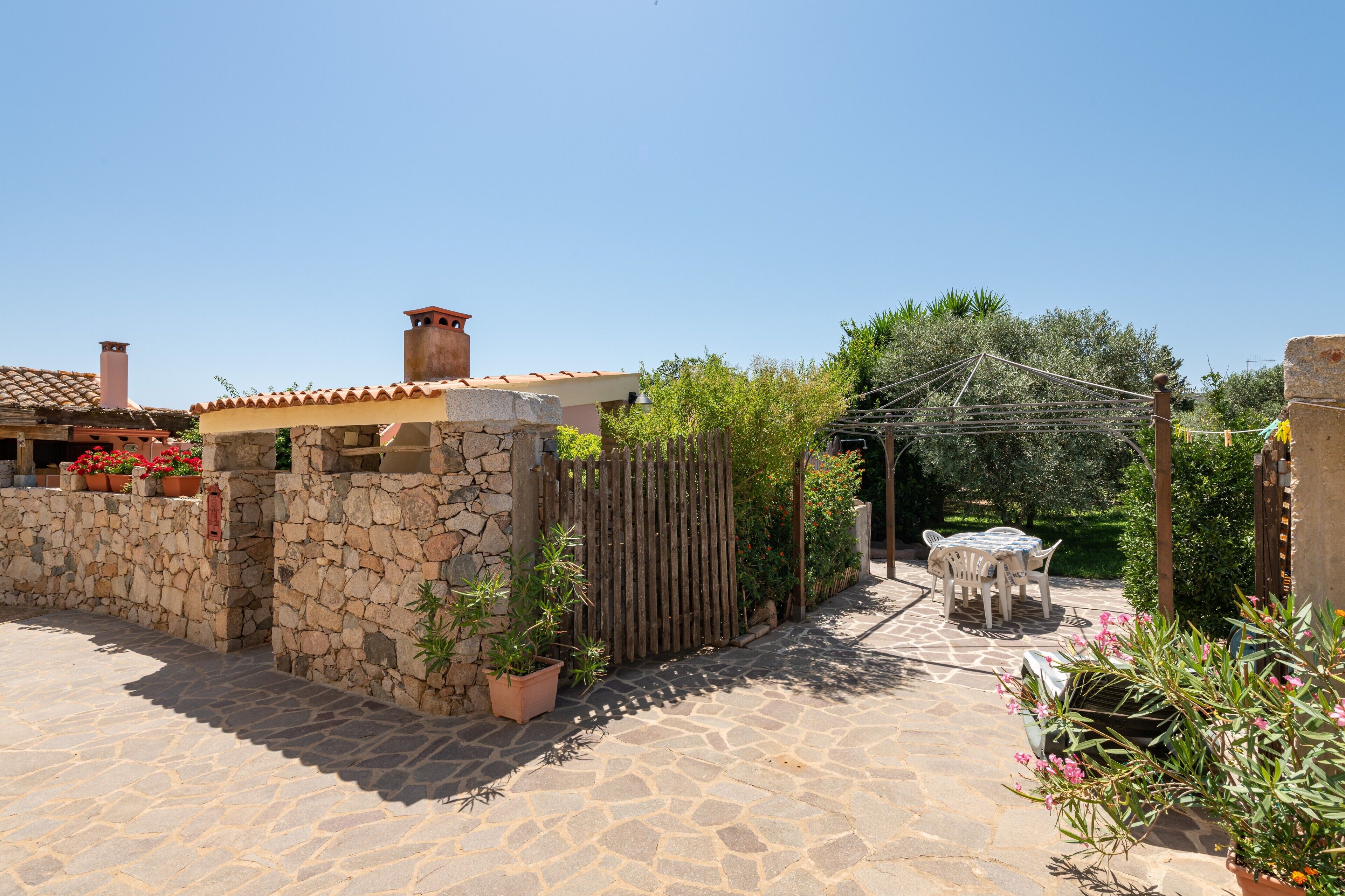 A stone patio with a wooden fence, a table with chairs, and potted plants.