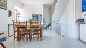 Ein Essbereich mit Holztisch und Stühlen, im Hintergrund eine Küche und eine Treppe, die zu einer oberen Ebene führt.