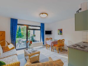 A room with a dining table, chairs, a sofa, a TV, and a kitchen area.