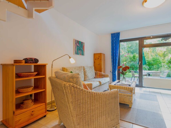 A living room with a sofa, wicker furniture, a wooden cabinet, and a view of greenery through a large window.