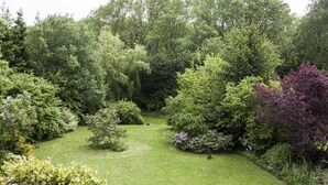 Ein üppiger Garten mit verschiedenen Bäumen und Sträuchern, einem gepflegten Rasen und einem kleinen Teich.