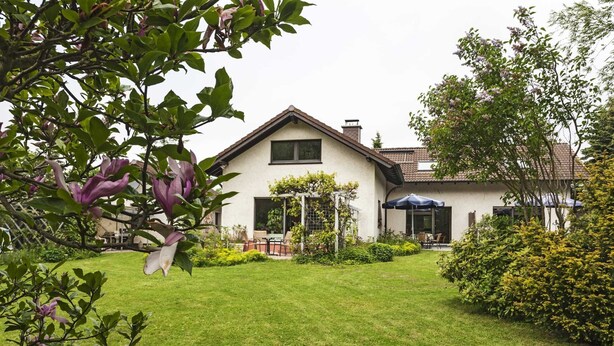 Ein Haus mit einem gepflegten Rasen, einer Terrasse mit Gartenmöbeln und einem Garten voller Pflanzen und Blumen.