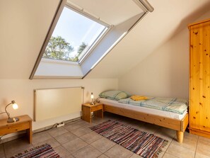A small, cozy bedroom with a sloped ceiling and skylight, a wooden bed, a nightstand, a desk, and a wardrobe.