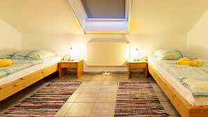 Ein kleiner, hell eingerichteter Raum mit zwei Einzelbetten, einem Dachfenster und einem großen Spiegel an der Wand.
