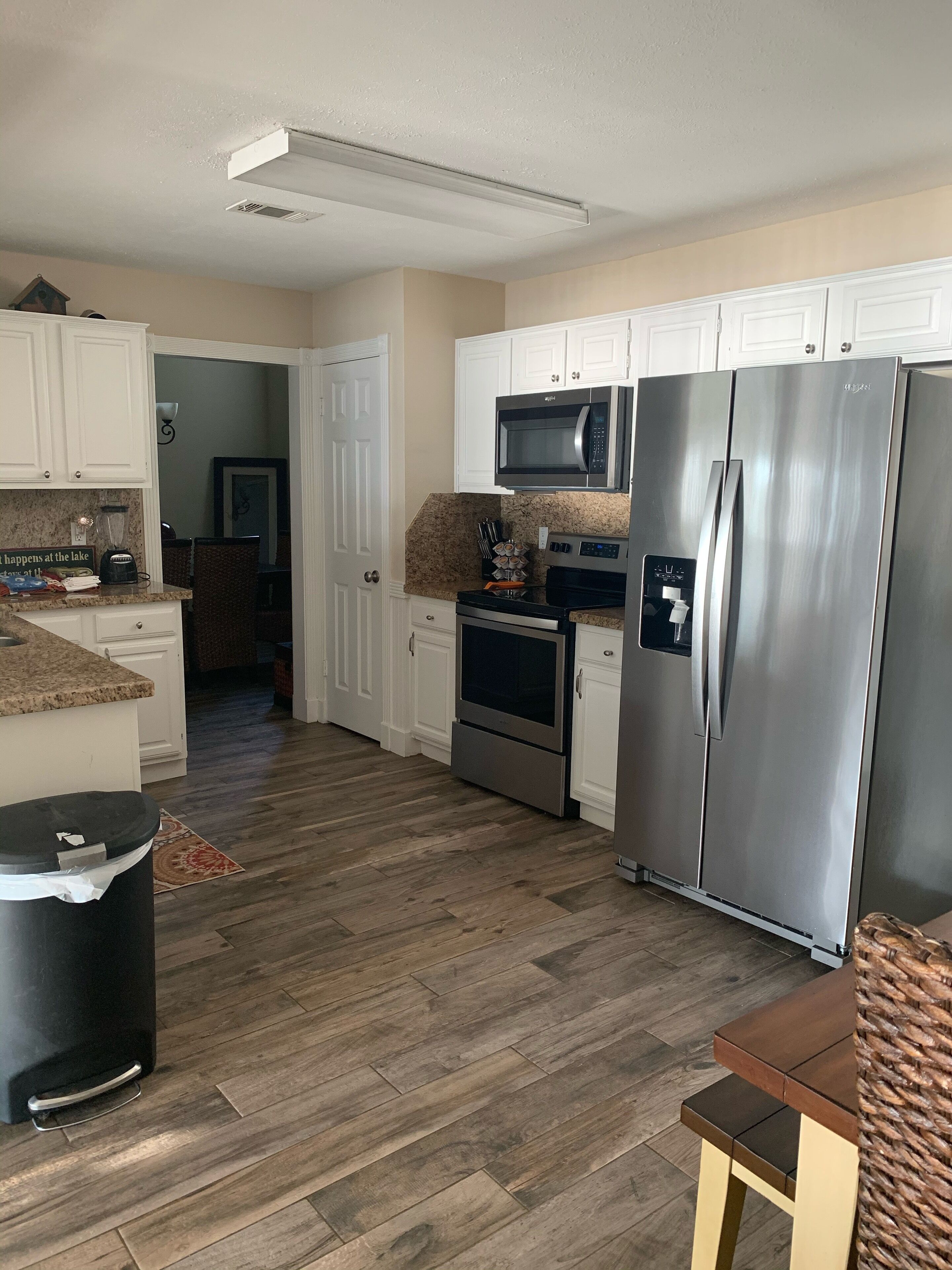 A modern kitchen with white cabinets, stainless steel appliances, and a herringbone wood floor.